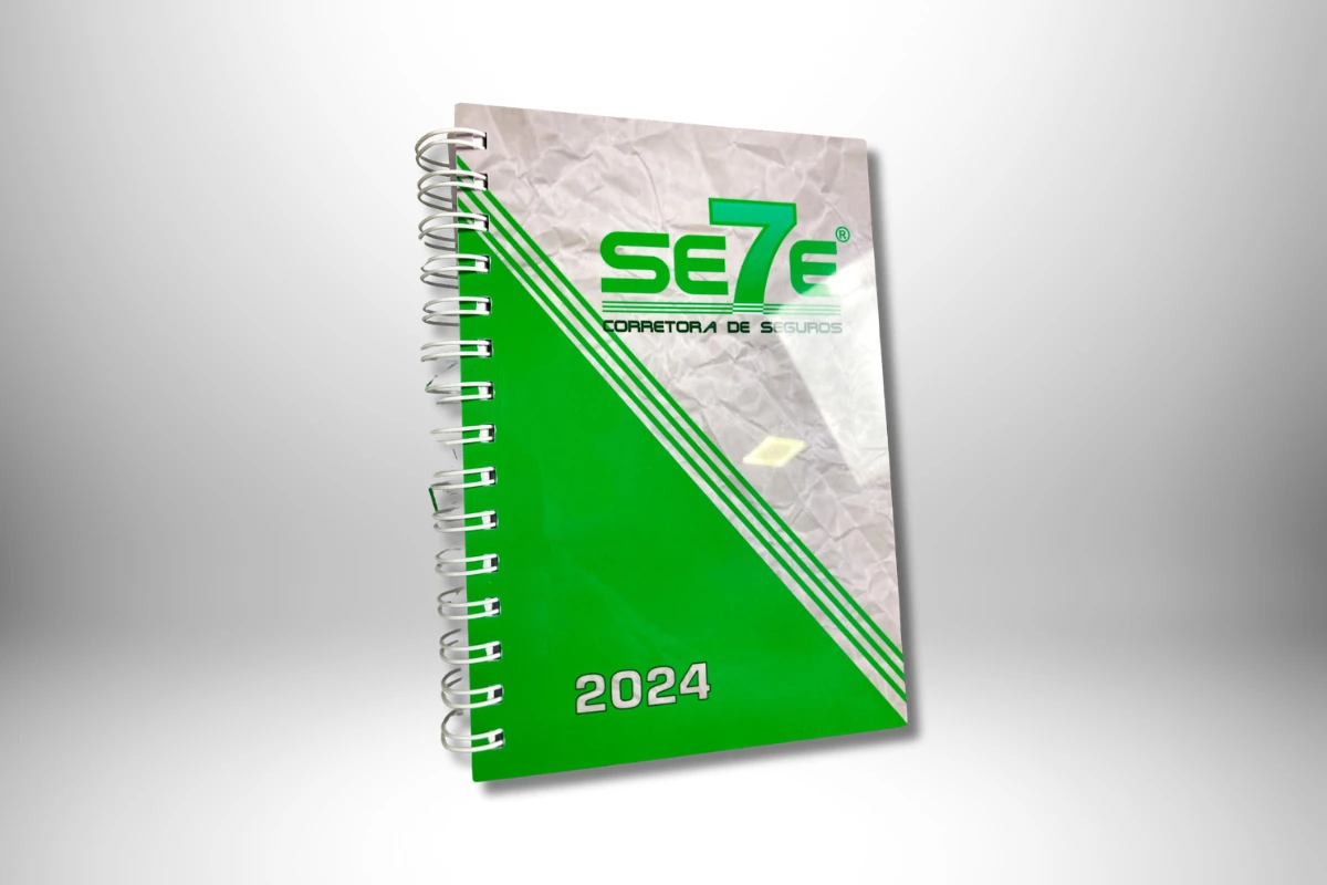 Agenda personalizada 2024 da Se7e Corretora de Seguros com capa verde e espiral metálico.