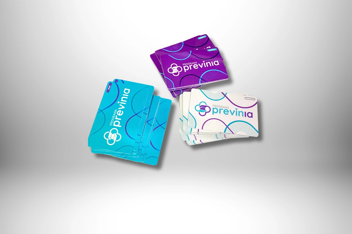 Cartões do Programa Previnia da Clínica da Cidade, nas cores azul, roxo e branco, organizados em três pilhas.